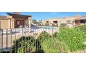 Community pool area with a covered patio, lush greenery, and a wrought iron fence at 4241 N Pebblecreek Pkwy # 54, Goodyear, AZ 85395