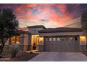 Exterior view of single-story home with decorative garage windows illuminated against a vibrant sunset sky at 13068 W Mine Trl, Peoria, AZ 85383