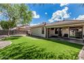 Lush backyard with artificial grass, mature trees, and a view of the patio featuring outdoor lighting at 8058 W Caron Dr, Peoria, AZ 85345