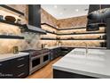 Modern kitchen with black cabinets, white countertops, stainless steel appliances, and wood-patterned accent wall at 5301 E Paradise Canyon Rd, Paradise Valley, AZ 85253