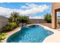 Inviting backyard oasis with a sparkling pool, rock waterfall feature, and lush tropical landscaping at 17358 N 185Th Ln, Surprise, AZ 85374