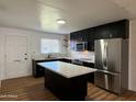 Well-lit kitchen features black cabinets, stainless steel appliances, island with quartz countertop, and updated backsplash at 7129 W Meadowbrook Ave, Phoenix, AZ 85033