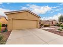 A tan home featuring a well-maintained yard, a two-car garage, and desert landscaping with green and flowering plants at 42911 W Magic Moment Dr, Maricopa, AZ 85138