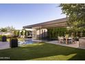 Expansive backyard showcasing a pool with a waterfall feature, outdoor dining, a kitchen, and lush green grass at 24283 S 219Th Way, Queen Creek, AZ 85142