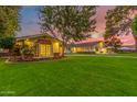 Charming home exterior featuring a manicured lawn, mature trees, and inviting outdoor lighting at dusk at 5801 E Exeter Blvd, Phoenix, AZ 85018
