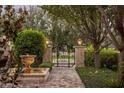 A walkway with an ornate fountain leads to an iron gate framed by stone pillars and lush landscaping at 5902 E Arcadia Ln, Phoenix, AZ 85018