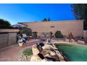 Poolside view featuring a rock waterfall, outdoor seating, and lush desert landscaping at 16857 E Deuce Ct, Fountain Hills, AZ 85268