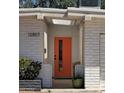 Close up of the entrance to the home with a bright orange front door, white brick and green potted plant at 12807 N 21St Dr, Phoenix, AZ 85029