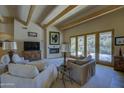 Inviting living room features beamed ceilings, fireplace, and desert views through French doors at 8619 E Silver Saddle Dr, Carefree, AZ 85377