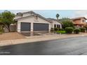 View of the home's exterior and three-car garage with low maintenance gravel and green grassy lawn at 6155 E Karen Dr, Scottsdale, AZ 85254