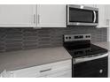 Close-up of kitchen details: grey backsplash, stainless steel stove, oven, microwave, white cabinets and light countertops at 17809 W Getty Dr, Goodyear, AZ 85338
