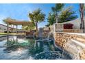 Stunning pool featuring beautiful waterfalls, a covered dining area, lush landscaping, and a tranquil backyard setting at 19888 E Russet Rd, Queen Creek, AZ 85142