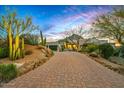 Expansive brick driveway leads to a secluded estate with lush desert landscaping and mountain views at 39912 N 98Th Way, Scottsdale, AZ 85262