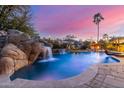 Lush backyard featuring a stunning pool with a rock waterfall, complemented by mature landscaping and a captivating twilight sky at 3353 E Nolan Dr, Chandler, AZ 85249