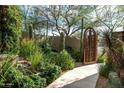 A lovely desert courtyard with unique iron gated entrance, mature landscaping, and stone walking path at 9722 E Mark Ln, Scottsdale, AZ 85262