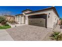 Home exterior showcasing a brick driveway, front yard, and warm beige stucco, creating an inviting curb appeal at 36053 N Stoneware Dr, Queen Creek, AZ 85140