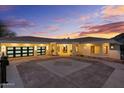 Elegant home featuring a spacious driveway, modern garage doors, grand pillars, and a beautifully lit entryway at dusk at 6602 N Arizona Biltmore Cir, Phoenix, AZ 85016