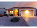 Inviting single-story home showcasing desert landscaping, an arched entrance, and warm exterior lights at sunset at 17805 W Arizona Dr, Surprise, AZ 85374