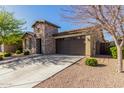 This beautiful house features a stone exterior, a two-car garage, and a well-manicured lawn at 22214 E Cherrywood Dr, Queen Creek, AZ 85142