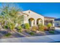 Charming single-story home featuring a desert landscape with colorful flowering bushes and a stucco exterior, with arched entryway at 5245 N 205Th Ln, Buckeye, AZ 85396