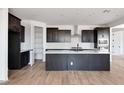 Modern kitchen features dark cabinets, an island, stainless steel appliances, and wood-look tile flooring at 16749 W Whispering Wind Dr, Surprise, AZ 85387