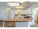 Well-lit kitchen boasts white cabinets, a breakfast bar, and modern appliances under a skylight at 7737 W Medlock Dr, Glendale, AZ 85303