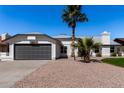 Single-story home showcasing a gray garage door, rock landscaping, and desert palm trees at 10934 E Becker Ln, Scottsdale, AZ 85259