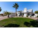 A single-story home boasts mature palm trees, a manicured lawn, and a charming white exterior at 10934 E Becker Ln, Scottsdale, AZ 85259