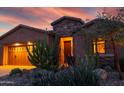 Exterior shot of a home with a stone facade entrance and desert landscaping, illuminated by twilight at 27654 N 125Th Dr, Peoria, AZ 85383