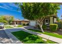 Charming house showcasing lush green lawns, a shade tree, and a driveway leading to a garage at 4059 E Mesquite St, Gilbert, AZ 85296