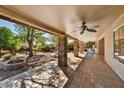 A spacious covered patio featuring brick columns, ceiling fan, and a landscaped backyard with a fire pit at 19021 N 90Th Ln, Peoria, AZ 85382