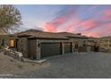 A spacious three-car garage with stone accents, set against a backdrop of a scenic desert landscape and beautiful sunset at 11320 N Crestview Dr, Fountain Hills, AZ 85268
