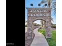 Rancho El Dorado community sign with stone archway and palm tree-lined street at 42370 W Hillman Dr, Maricopa, AZ 85138