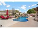 Backyard oasis featuring a luxurious pool, rock waterfall, spa, and desert landscaping at 6372 W Hill Ln, Glendale, AZ 85310