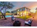 Serene backyard featuring a fire pit and swing set enhanced with landscape lighting for cozy outdoor enjoyment at 12229 N 121St Dr, El Mirage, AZ 85335