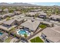 A high angle view showcases a residence with a private pool, spa, patio, green grass, and mountain views at 18120 W Cassia Way, Goodyear, AZ 85338
