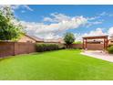 Expansive backyard featuring lush artificial turf, a brick perimeter wall, and a covered patio with string lights at 1437 E Flamingo Way, Gilbert, AZ 85297