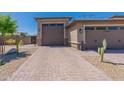 A three-car garage boasts neutral paint, desert landscaping, and a brick driveway under a cloudless sky at 18159 W Piro St, Goodyear, AZ 85338