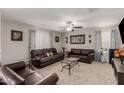 Spacious living room with leather sofas, patterned drapes, ceiling fan, and carpeted floors at 8046 W Agora Ln, Phoenix, AZ 85043