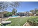 Expansive backyard featuring a refreshing pool, inviting firepit, lush artificial grass, and mature trees at 1853 W Estrella Dr, Chandler, AZ 85224