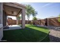 Secluded backyard with artificial turf, gravel beds, mature tree, covered patio, and desert-style fireplace at 20222 N 267Th Ln, Buckeye, AZ 85396