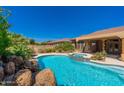 Backyard pool and spa with rock waterfall feature, lush landscaping, and covered patio area at 18575 E Pine Barrens Ave, Queen Creek, AZ 85142