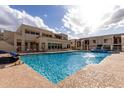 Community pool with seating surrounded by bright multi-story residential buildings under partly cloudy skies at 5518 E Lindstrom Ln # 3012, Mesa, AZ 85215