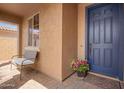 Inviting front porch with a blue door, a chair, a welcome mat, and plants, creating a charming entrance at 14390 W Desert Flower Dr, Goodyear, AZ 85395