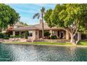 Beautiful waterfront backyard with a stone patio, lush lawn, mature trees, and outdoor seating area at 1833 W Mead Pl, Chandler, AZ 85248