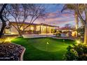 Expansive backyard features a putting green, stone landscaping, lush greenery, and a sparkling pool with a rock waterfall at 911 E Desert Inn Dr, Chandler, AZ 85249