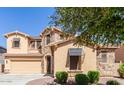 Tan home with stone accents, awning and a well-manicured lawn featuring mature trees at 15620 W Cameron Dr, Surprise, AZ 85379