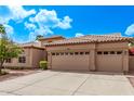 Tan home showcasing desert landscaping, a three-car garage, and a charming tiled roof under a bright blue sky at 1777 W Redfield Rd, Gilbert, AZ 85233