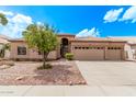 Tan home showcasing desert landscaping, a three-car garage, and a charming tiled roof under a bright blue sky at 1777 W Redfield Rd, Gilbert, AZ 85233