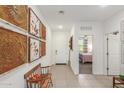 Bright hallway with decorative wall art, bench, and tiled flooring, leading to a bedroom and the front door at 17971 W Meadowbrook Ave, Goodyear, AZ 85395